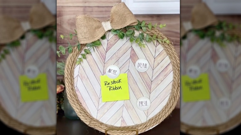A magnet holds the note "Restock Ribbon" onto a farmhouse-style magnet board resting in a plate holder.