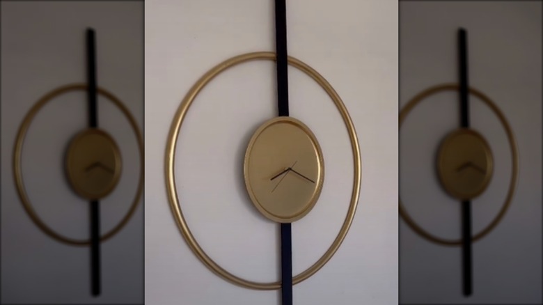 Two gold floating concentric circles are held together by a thin black board to create a modern wall clock.