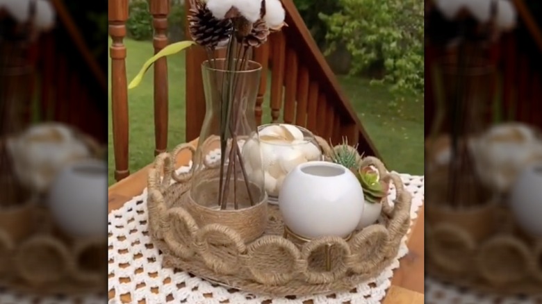 A tray covered in nautical rope features a raised border of rope rings and hold various decorative items on an outdoor table.