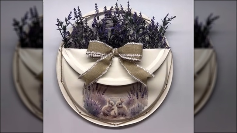 A decorative spring wreath has a pocket that holds dried purple flowers.