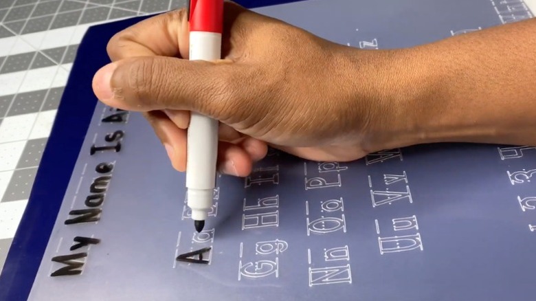 A person using marker with alphabet tracing mat made from Dollar Tree chopping mat