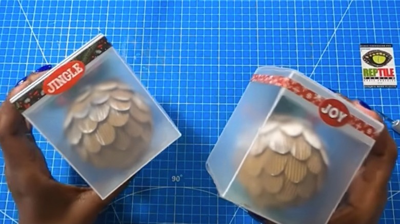 A person holding two Christmas ornament display boxes made from Dollar Tree chopping mats