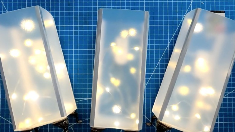Three DIY luminaries made from Dollar Tree chopping mats lying on cutting mat