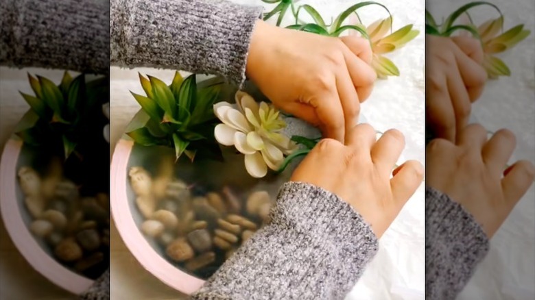 A person making imitation wall-hanging planter with river rocks and imitation greenery