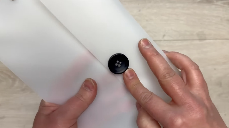 A person closing button clasp on DIY clear plastic envelope made from Dollar Tree chopping mat