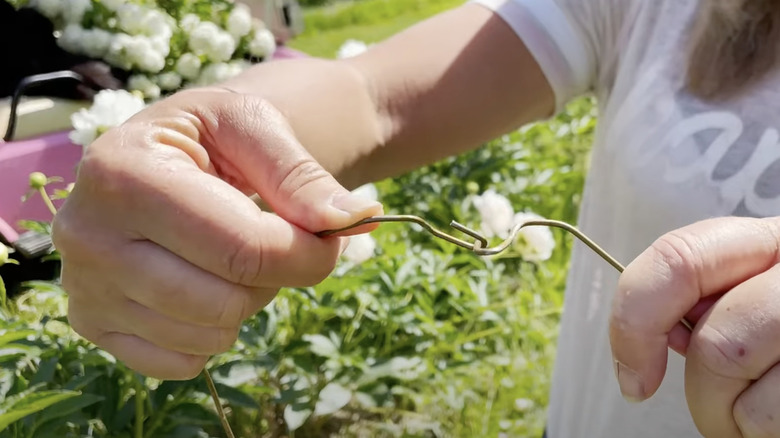 A woman connects two wire clothes hangers together at their hooked ends.