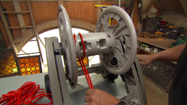 A man prepares to wrap an air compressor hose around an old garden hose reel.