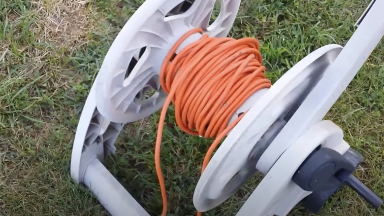 A long extension cord has been wound around an old garden hose reel.