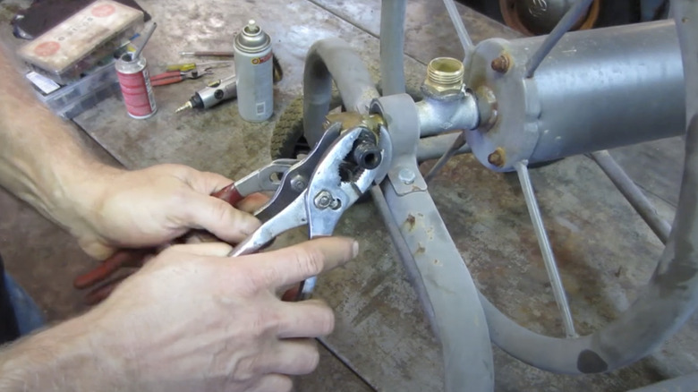 A person repairs a metal garden hose reel with pliers and other tools and supplies.