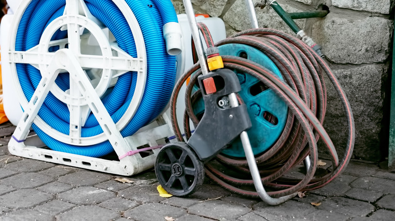 Multiple garden hoses hang or are wound around a garden hose reel in front of a shed.