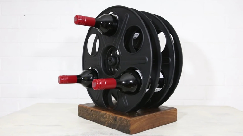 A wine rack constructed from an old garden hose reel and a piece of scrap wood.