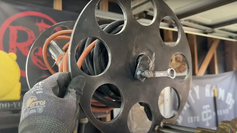 Welding cables are wound around the spool of an old garden hose reel.