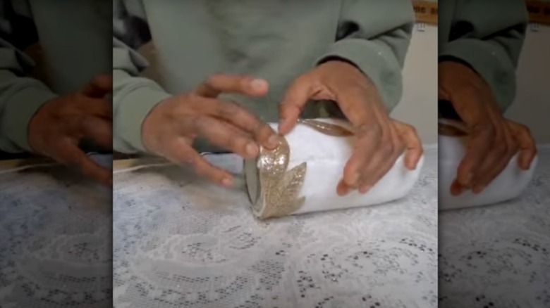 A woman holds a vase she made using imitation foliage and a white microfiber cloth wrapped around a jar