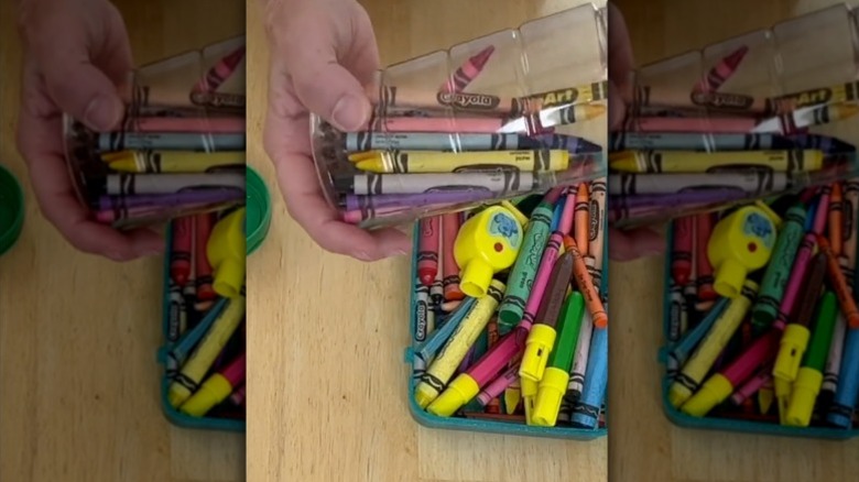 A hand holds a parmesan cheese container filled with crayons.