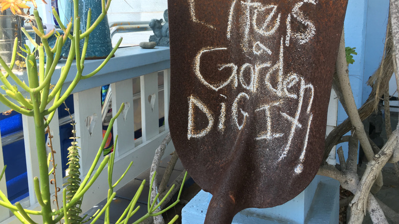 "Life is a Garden. Dig it!" written on a rusty shovel blade in chalk and stuck into the garden.