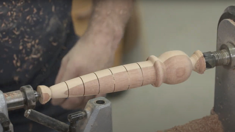 Turning an old shovel handle on a woodworking lathe to create a dibble.