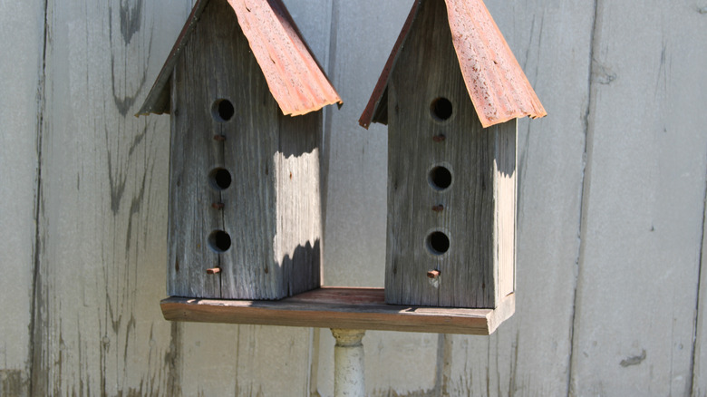 Two wooden birdhouses affixed to a wooden plank that sits atop a repurposed wooden shovel handle.