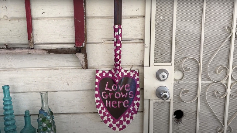 A painted shovel hung on the wall as garden art.