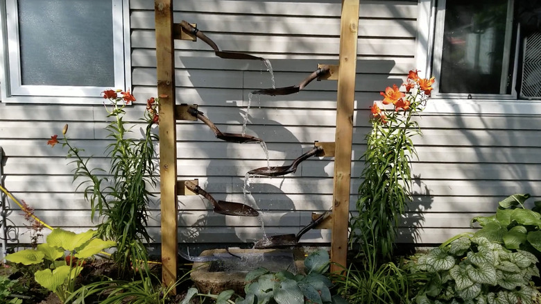 Water cascades down multiple shovel heads fitted into two parallel wooden posts in the garden.