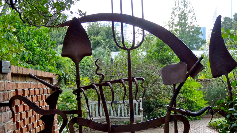 A shovel and other old metal garden tools form the bars of a whimsical garden gate.
