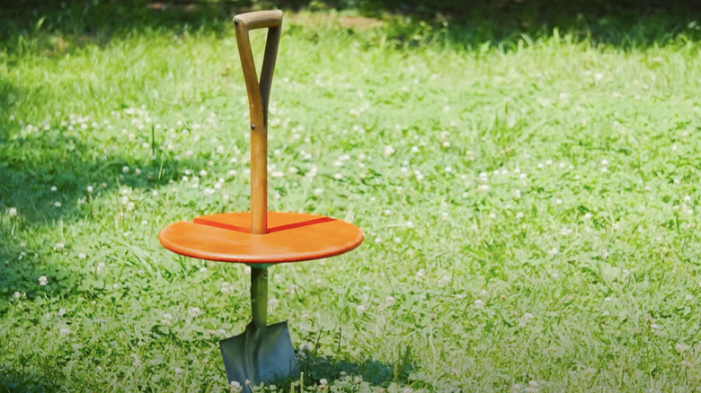 A portable garden table made from a red painted wood round and an old shovel.