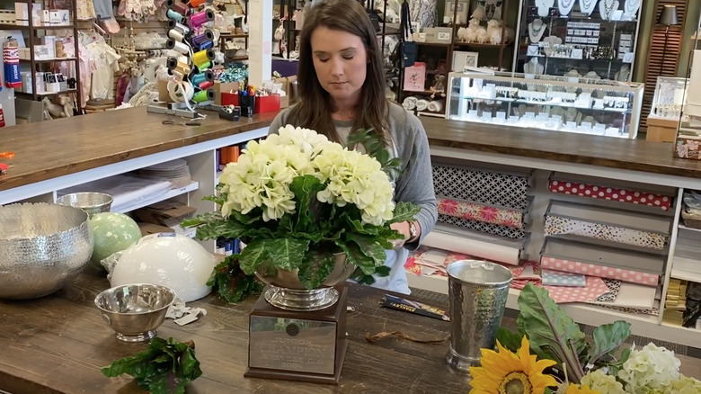 a woman putting white artificial flowers into a bowl trophy
