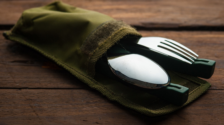 An olive green silverware pocket sitting on a wooden table.
