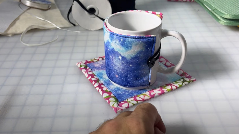 A square mug rug coaster and a mug rug sweater sitting on a craft table.