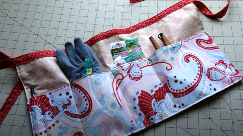 A DIYed garden apron with several pockets filled with vegetable seeds, gloves, and clippers.