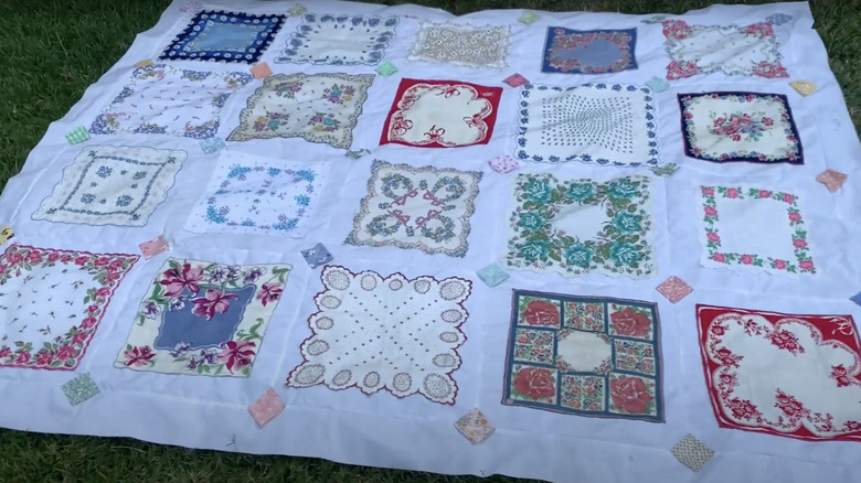 A quilt made from vintage handkerchiefs is laid out on the grass in the backyard.