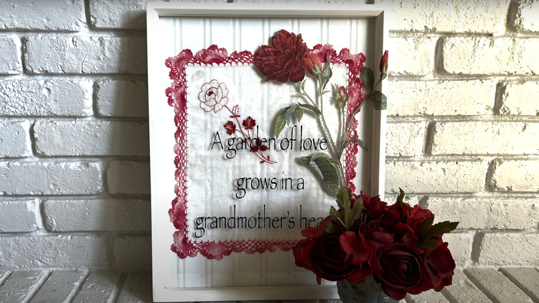 A handkerchief in a frame with some flowers and a sweet phrase.