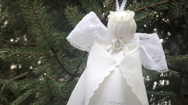 An angel ornament made from a white vintage handkerchief hangs from a branch on a Christmas tree.