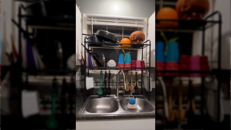 A black metal shelving rack over a kitchen sink and used as a drying rack and cooking utensil holder.