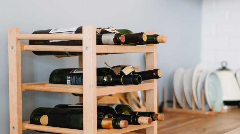 A three-tiered wooden rack used to store wine bottles, placed on a kitchen countertop.
