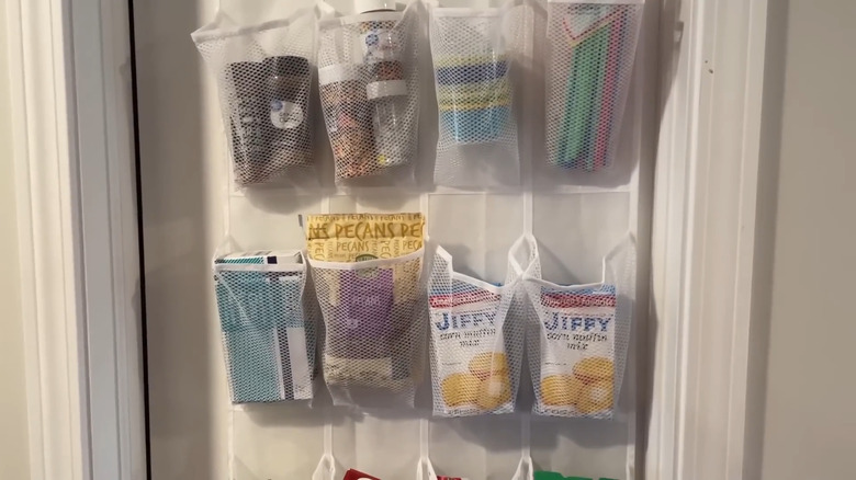 An over-the-door white mesh shoe organizer filled with candy, seasonings, and boxed cake mixes.