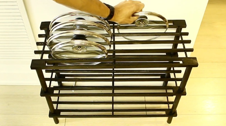 A wooden shoe rack painted black and used to store cooking pot lids.