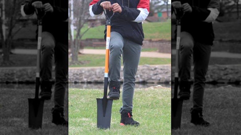 A person stands with their foot on the head of a trenching shovel.