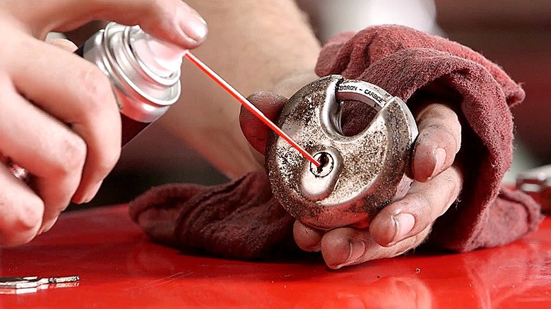 Close-up of a hand spraying 3-in-One into the mechanism of a padlock