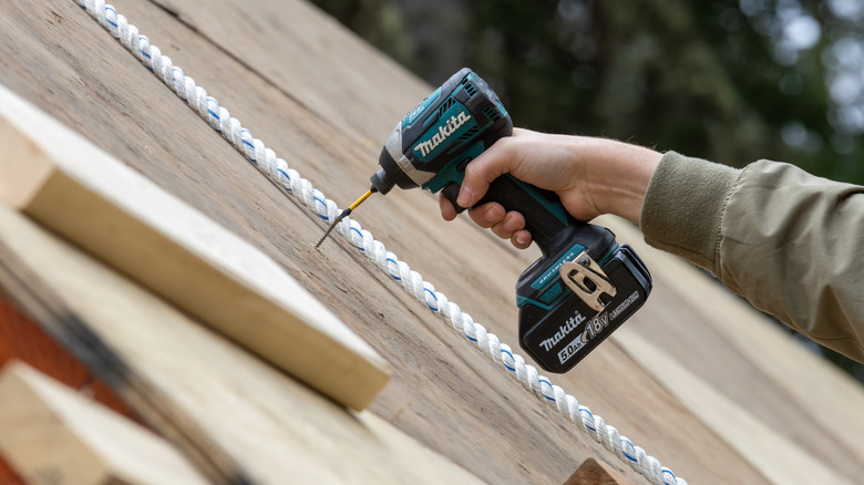 Hand using a Makita impact driver to tighten screws on a roof