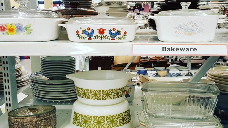 An assortment of Pyrex and CorningWare pieces on shelves at a thrift store