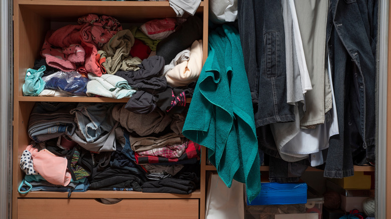 clutter in a clothing closet, hanging pants, and shelves full of clothes stuffed into place