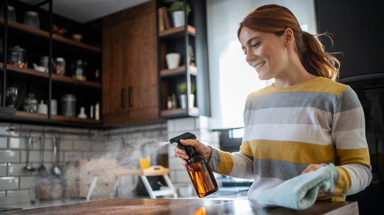 Woman smiling and spraying cleaner over kitchen countertop
