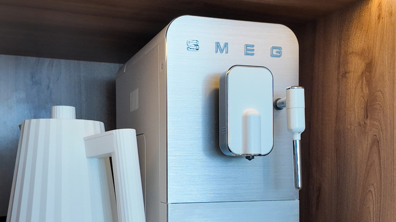 A white Smeg coffee machine in a cupboard next to a white kettle.