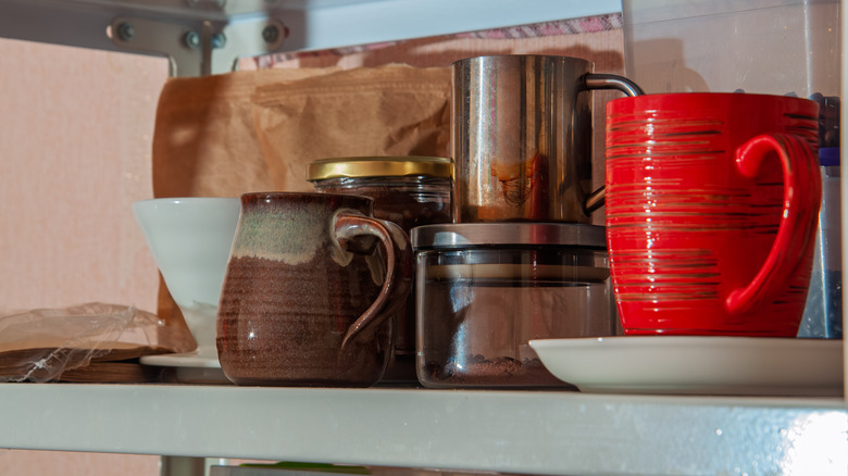 A cupboard shelf with coffee grounds and coffee mugs.