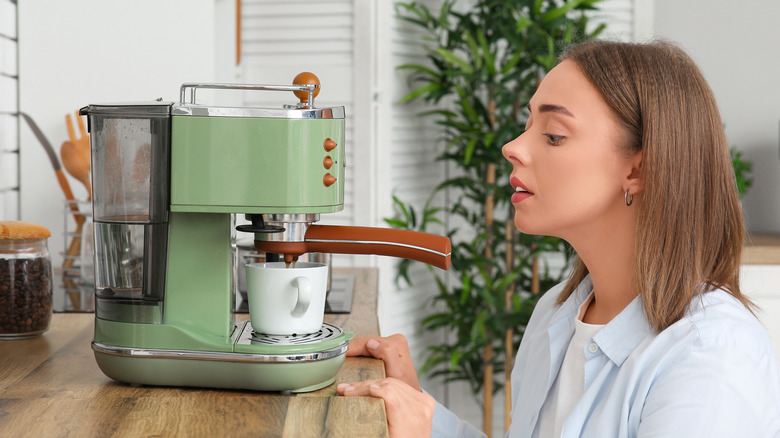 A young woman making coffee in an elegant green coffee machine.