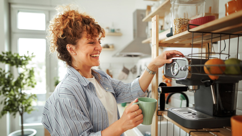 A young woman making coffee with a machine that's situated below containers with cereal and food in.