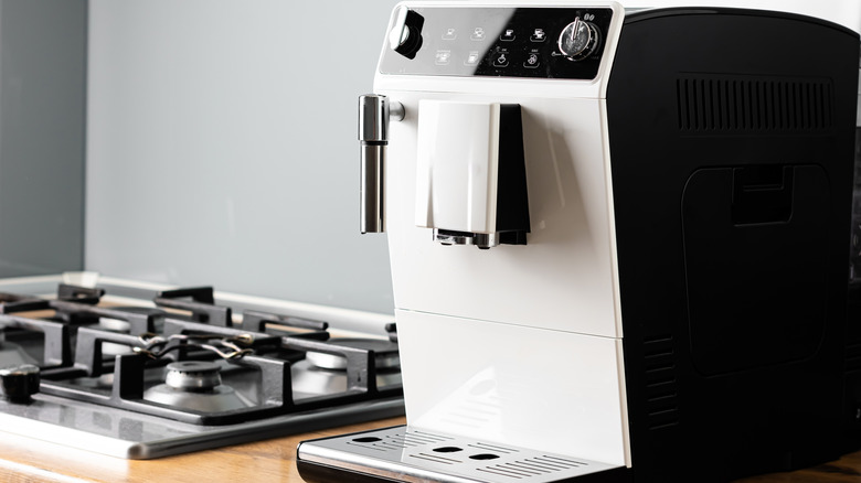 A large white coffee machine next to a gas chrome hob.
