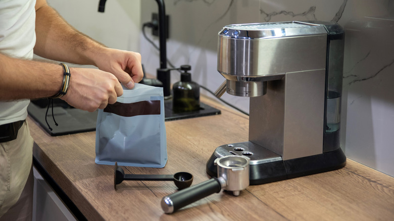 A coffee machine on a wooden work surface with a man opening a bag of coffee.