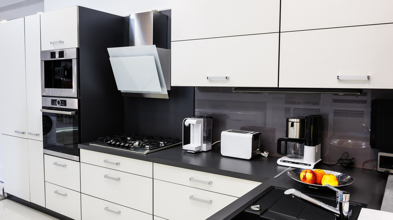 A modern white kitchen with integrated oven and hob, with toaster and coffee machines underneath the cabinets.