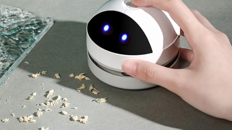 Hand holding a small white robot vacuum on a dirty desk